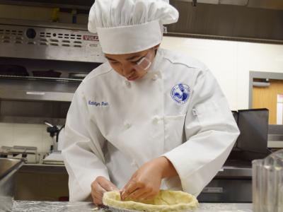 Student demonstrating pastry preparation in the Culinary Arts lab kitchen. 